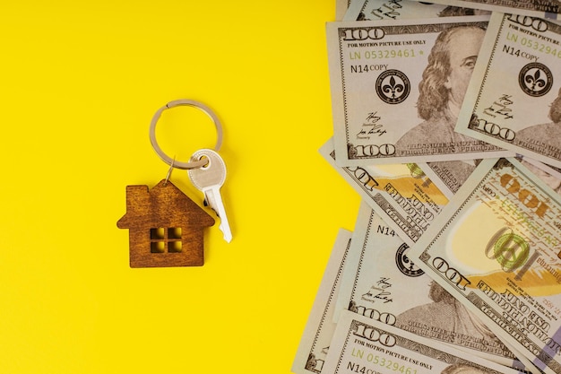 Chiave di casa con una piccola casa e dollari su sfondo giallo Il concetto di affittare o vendere casa