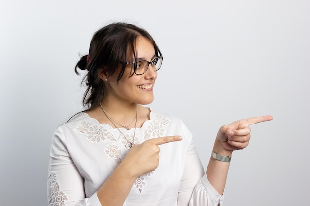 Chica joven sobre un fondo bianco sonriendo mientras senala hacia un lado