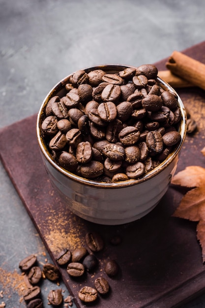 Chicchi di caffè ad alto angolo in tazza sul tagliere con cannella