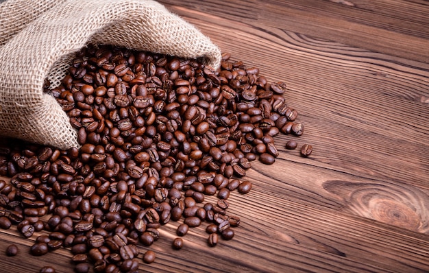 Chicchi di caffè arrostiti che svegliano da una borsa del caffè della iuta su una tavola di legno.