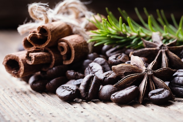 Chicchi di caffè con bastoncini di cannella, anice, ramo di abete sulla superficie in legno.