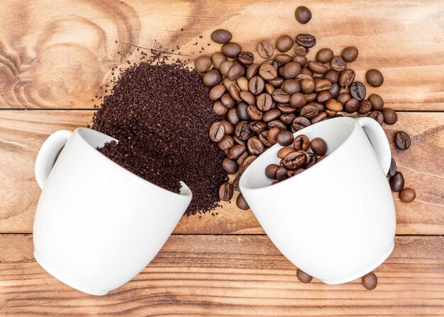 Chicchi di caffè con caffè macinato sparsi dalle tazze sul tavolo di legno Vista dall'alto