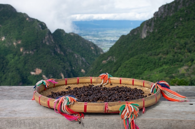 Chicchi di caffè crudi seccati al sole su una tavola di legno con i bei Mountain View in Tailandia del Nord.