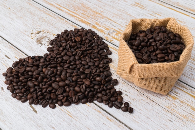 Chicchi di caffè disposti a forma di cuore e sacchetto di caffè su fondo di legno chiaro