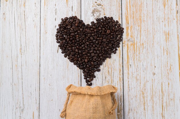 Chicchi di caffè disposti a forma di cuore su fondo di legno chiaro