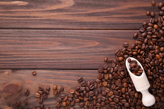 Chicchi di caffè in cucchiaio di legno su fondo marrone.