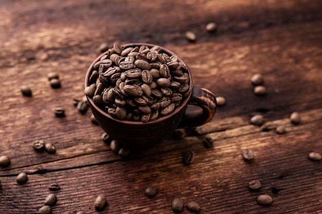 Chicchi di caffè in una tazza di argilla su un vecchio fondo di legno marrone.