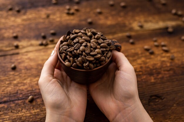 Chicchi di caffè in una tazza in mani femminili su uno sfondo marrone.