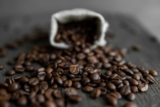 Chicchi di caffè sparsi da un sacchetto di lino su un tavolo Chicchi di caffè arabica freschi su tessuto di lino