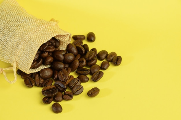 Chicchi di caffè sparsi da una piccola borsa su uno sfondo giallo sul lato sinistro.