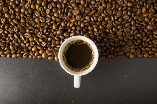 Chicchi di caffè su sfondo nero con una tazza bianca