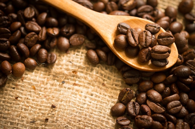 Chicchi di caffè su tela di sacco e su un cucchiaio di legno.