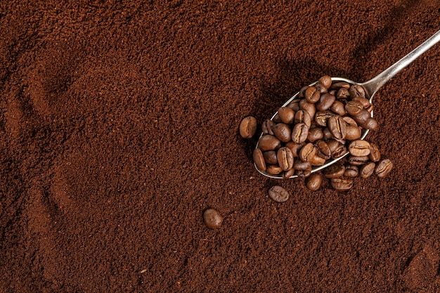 Chicchi di caffè sul cucchiaio sul fondo del caffè macinato. Avvicinamento.