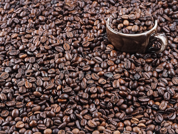 Chicchi di caffè tostati. Caffè scuro aromatico fresco. Una tazza marrone per caffè espresso si trova in chicchi di caffè. Avvicinamento.