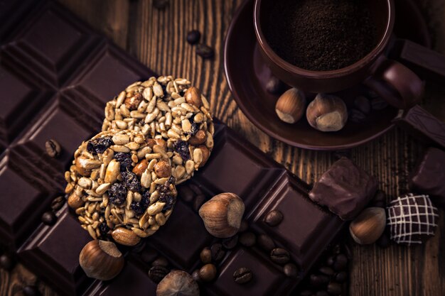 Chicchi di caffè tostati, cioccolato, muesli, caramelle, noci e tazza sulla superficie in legno