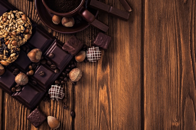 Chicchi di caffè tostati, cioccolato, muesli, caramelle, noci e tazza sulla superficie in legno