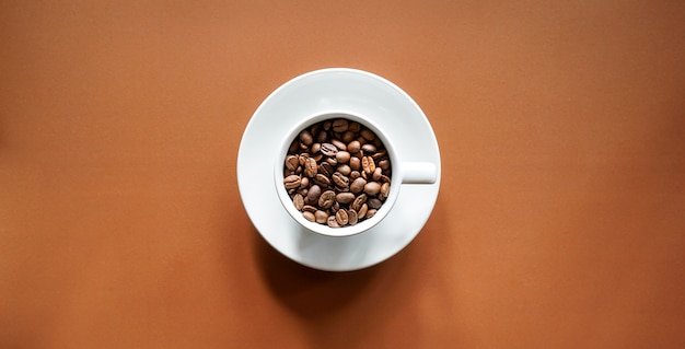 chicchi di caffè tostati in tazza di caffè bianco con sfondo marrone