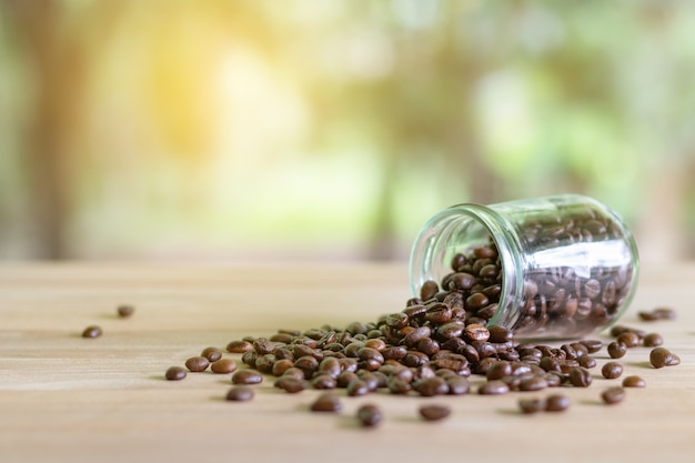 Chicchi di caffè tostato in bottiglie di vetro immessi sul tavolo con sfondo di natura.