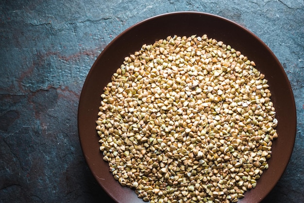 Chicchi di grano saraceno verde su un piatto di ceramica marrone su una pietra blu