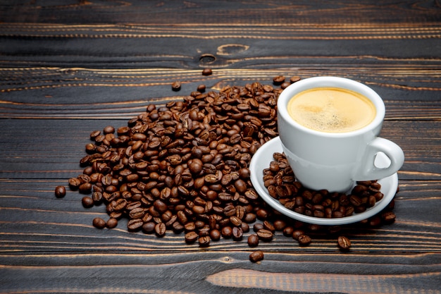 Chicchi e tazza di caffè arrostiti su fondo di legno