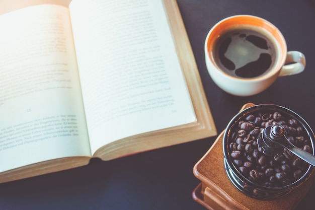 Chicco di caffè del fuoco selettivo in smerigliatrice d&#39;annata con la tazza di caffè e libro sulla tavola