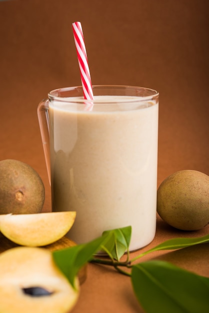 Chickoo, Chikoo O Sapota Milkshake gustoso e salutare. È un frutto sano mescolato con latte e ghiaccio servito in un bicchiere su uno sfondo colorato o in legno. Messa a fuoco selettiva