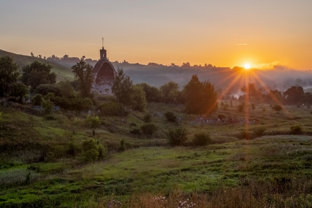 Chiesa dell'Arcangelo Mikhail Sun con raggi Mattinata nebbiosa villaggio Kocherginka Russia