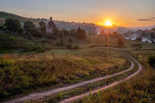 Chiesa dell'Arcangelo Mikhail Sun con raggi Mattinata nebbiosa villaggio Kocherginka Russia