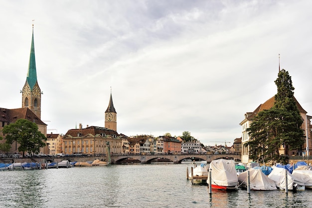 Chiesa di Fraumunster e San Pietro e barche al molo del fiume Limmat nel centro della città di Zurigo, Svizzera. Persone sullo sfondo