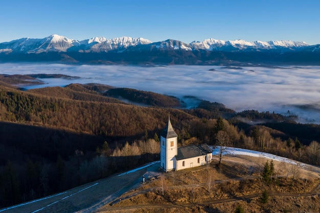 Chiesa di San Primoz e Felicijan in una giornata di sole sopra le nuvole Alpi Giulie Jamnik Slovenia Europa Veduta aerea