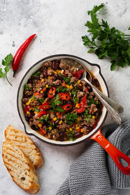 Chili con carne con carne macinata e verdure in umido in salsa di pomodoro in una padella di ghisa su ardesia grigio chiaro o superficie in cemento