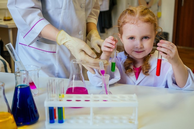 Chimica della ragazza della scuola dai capelli rossi intelligente in occhiali e abito medico bianco che fa esperimenti scientifici di chimica, mescolando diverse soluzioni chimiche nell'aula di laboratorio