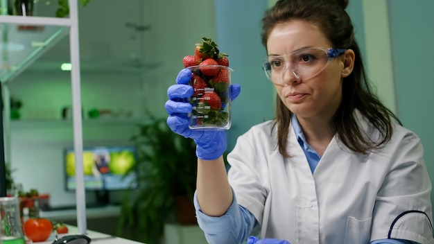 Chimico che digita competenza botanica medica su computer per esperimento agricolo che analizza il vetro con fragole organiche alla ricerca di mutazioni genetiche. Ricercatore botanico che lavora nel laboratorio di agricoltura