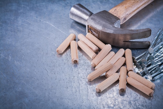 Chiodi della costruzione del martello da carpentiere e tasselli di legno sul concetto di manutenzione del fondo metallico graffiato