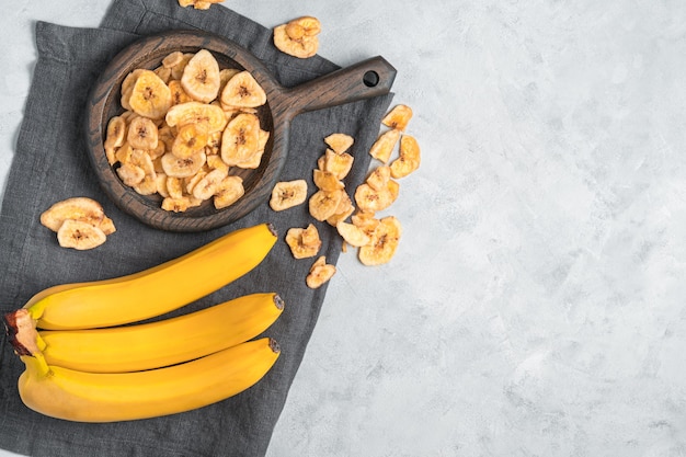 Chip di banana naturali e fatti in casa e banane fresche su un muro grigio. Vista dall'alto, copia dello spazio.