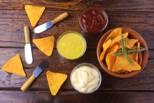 Chip di mais nachos disposti in ciotola di ceramica sul tavolo di legno accanto a salse assortite