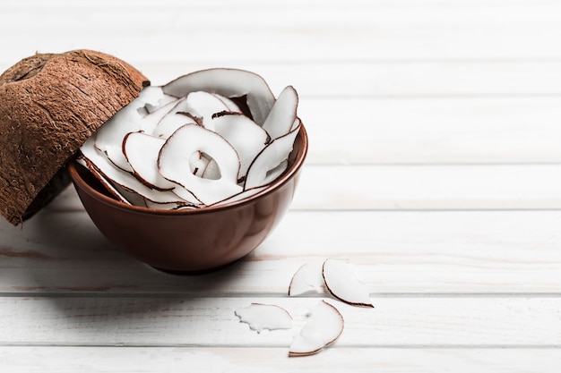 Chip di noce di cocco in una ciotola marrone su un bianco di legno