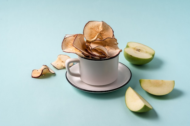 Chip secchi della mela in una tazza e mele fresche sopra blu-chiaro.