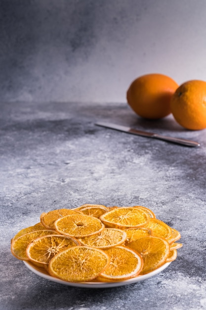 Chips di arance secche nel piatto e frutta fresca di arancia con coltello