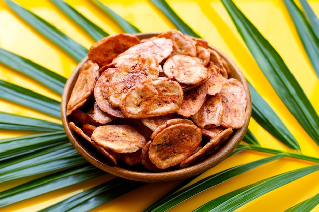 Chips di banana in una ciotola di legno su foglie di palma sulla superficie gialla