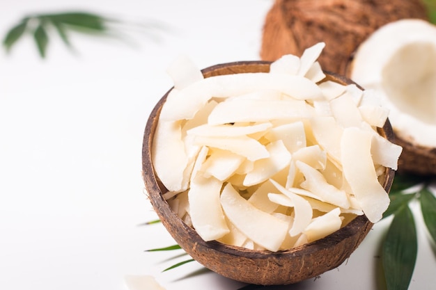 Chips di cocco con cocco e foglie verdi su sfondo bianco. Concetto isolato.