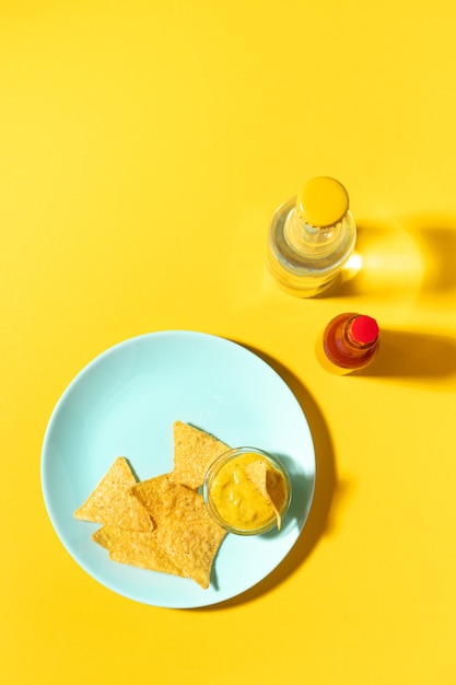 Chips di nachos con salsa di formaggio sul piatto blu su giallo