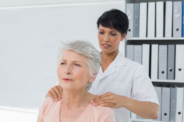 Chiropratico femminile che massaggia la spalla di una donna senior nell&#39;ufficio medico