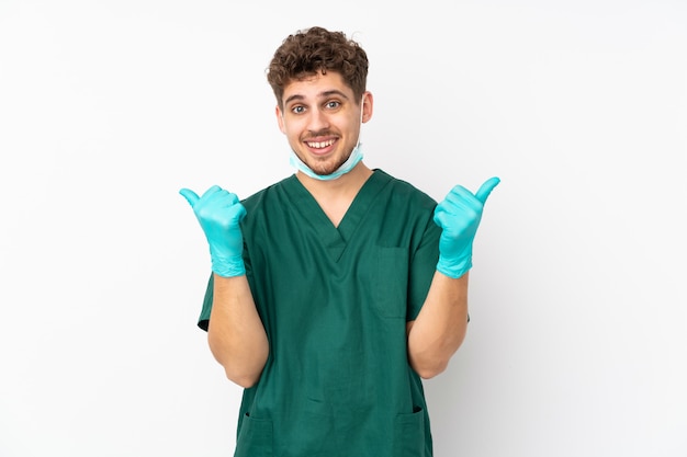 Chirurgo in uniforme verde sulla parete bianca con pollice in alto gesto e sorridente