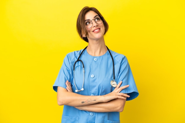 Chirurgo medico donna isolata su sfondo giallo guardando in alto mentre sorride