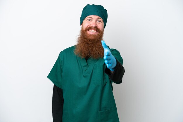 Chirurgo redhead uomo in uniforme verde isolato su sfondo bianco stringe la mano per chiudere un buon affare