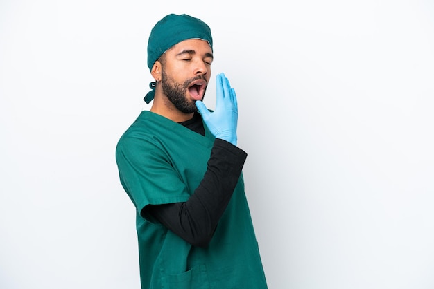 Chirurgo uomo brasiliano in uniforme verde isolato su sfondo bianco che sbadiglia e copre la bocca spalancata con la mano