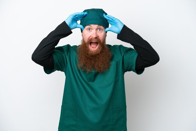 Chirurgo uomo rosso in uniforme verde isolato su sfondo bianco con espressione sorpresa