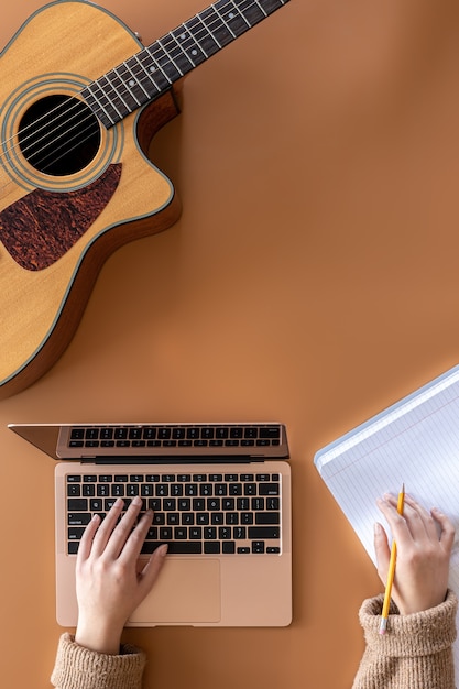 Chitarra acustica, mani femminili lavorano dietro un laptop, il concetto di creazione di musica.