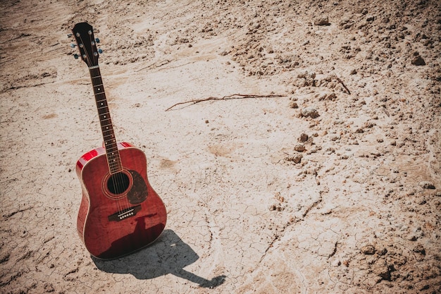 Chitarra acustica sdraiata su uno stile vintage di terra deserta con spazio di copia